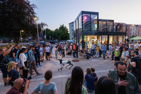 Foto vom Vorplatz am Barkhausen-Bau der TU Dresden. Um einen Roboterhund hat sich einen Menschenmenge gebildet, die das Treiben begutachtet.