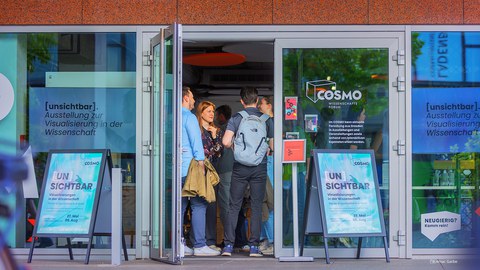 In den geöffneten Türen des COSMO Forums stehen mehrere Menschen dicht egedrängt, um EInlass zu erhalten. 