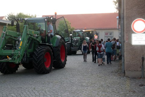 Ein hoher Traktor fährt über Pflastersteine auf dem TUD Campus. Eine Gruppe junger Menschen läuft an ihm vorbei.