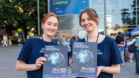 Foto von zwei Frauen, die vor dem HSZ der TU Dresden, Plakate zur Langen Nacht der Wissenschaften halten.
