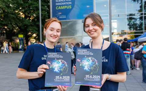 Foto von zwei Frauen, die vor dem HSZ der TU Dresden, Plakate zur Langen Nacht der Wissenschaften halten.