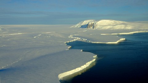 Ausflussgletscher in der Pine-Island-Bucht (Westantarktis) (Hintergrund) mit vorgelagertem aufschwimmenden Schelfeis (Vordergrund). Wechselwirkungen des Gletschers mit dem Ozean und dem festen Untergrund führen dazu, dass sich das Eis beschleunigt bewegt.
