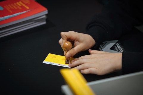 Foto von den Händen einer Person, die gerade einen Stempel auf eine Stempelkarte der Kinder-Uni hinzufügt.