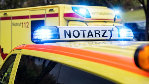 Foto von einem Notarzt und einem Rettungswagen. Bei beiden Fahrzeugen ist das Blaulicht angeschaltet.