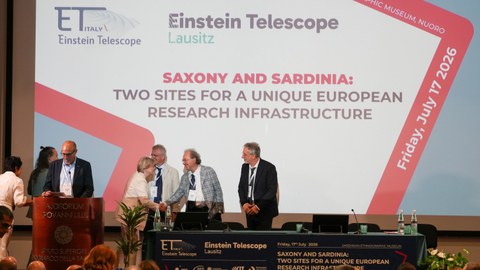 Foto von mehreren Personen, darunter Prof.in Angela Rösen-Wolff von der TU Dresden, die gerade eine Bühne betreten und sich begrüßen.