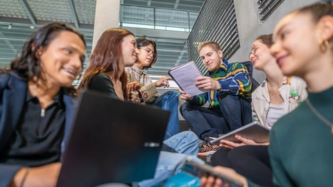 A photo of six students sitting on some steps on the TUD campus, studying together. 