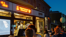 Bei Dunkelheit steht eine Menschengruppe vor einer gelben Straßenbahn der DVB, deren Display „Lange Nacht der Wissenschaft“ anzeigt. Im Inneren der Bahn laufen technische Vorführungen, die durch das Fenster sichtbar sind. Menschen unterhalten sich, ein Kind hält einen Luftballon.