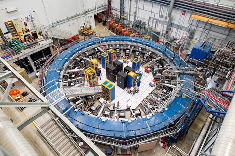 Blick auf den blauen Muon g-2 Ring, er befindet sich in seiner Detektorhalle inmitten von Elektronikregalen, der Myonen-Beamline und anderen Geräten.