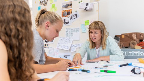 Studentinnen und ihre Betreuerin sitzen an am Tisch und arbeiten an einem Projekt