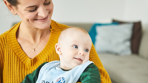 Links sitzt eine lächelnde Frau, auf deren Schoß sitzt ein Baby.