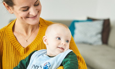 Links sitzt eine lächelnde Frau, auf deren Schoß sitzt ein Baby.