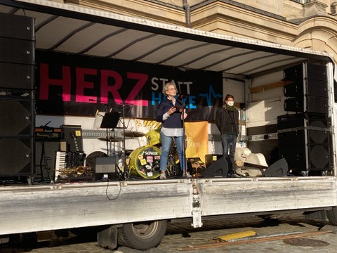 Eine Frau steht auf einer Bühne und spricht in ein Mikrofon, das vor ihr steht.