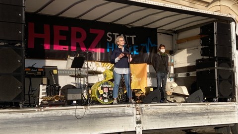 Eine Frau steht auf einer Bühne und spricht in ein Mikrofon, das vor ihr steht.