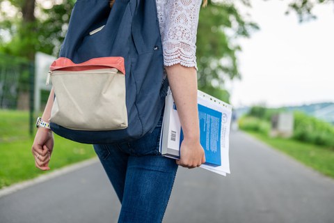 Eine Studentin spaziert am Blauen Wunder Dresden. Sie trägt einen blauen Rucksack auf dem Rücken und hält Hefter und Buch in der rechen Hand.