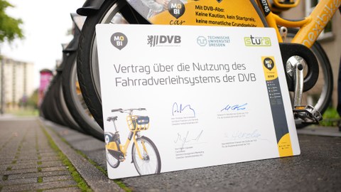 Symbolischer Vertrag zwischen TUD und DVB vor einer Reihe gelber Fahrräder.