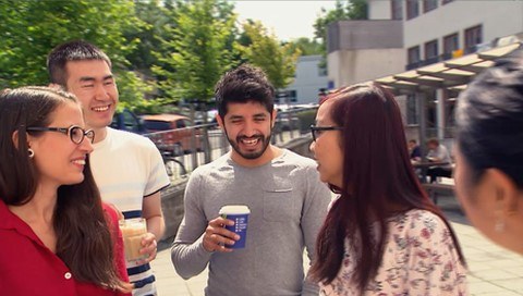 Junge Menschen verschiedener Nationalitäten trinken gemeinsam einen Kaffee auf dem Campus