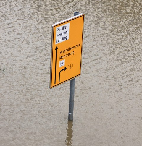 Ein Straßenschild/Wegweiser steht in einer Wassermasse.