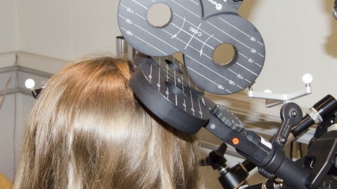 Ein Messgerät in schwarz mit weißer Beschriftung wird von oben rechts an einen blonden Haarschopf gedrückt.