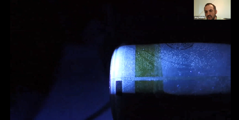 Auf schwarzem Hintergrund ist oben rechts ein kleines Foto des Referenten zu sehen, darunter größer eine blaue Flasche, auf der man Fingerabdrücke sieht.
