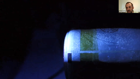 Auf schwarzem Hintergrund ist oben rechts ein kleines Foto des Referenten zu sehen, darunter größer eine blaue Flasche, auf der man Fingerabdrücke sieht.
