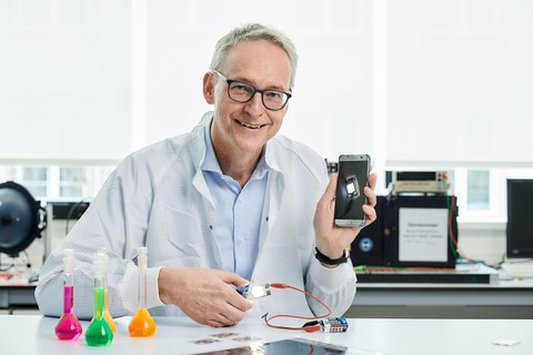 Porträtfoto Prof. Leo, er lächelt und hält ein Handy in die Kamera.