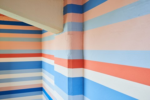 Verschiedene durchlaufende Farbstreifen (weiß, lachs, blau) an einer Wand.