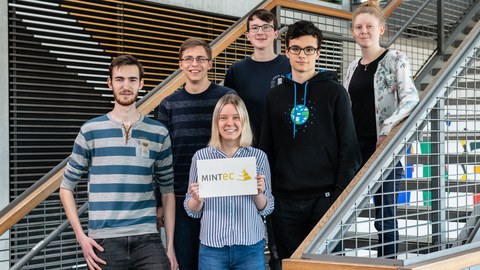 Gruppenbild mit sechs jungen Männern und Frauen, die in drei Reihen hintereinander auf einer Treppe stehen.