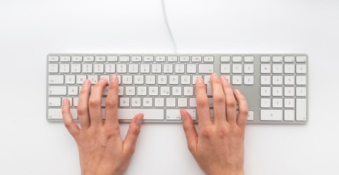 Eine rechte und eine linke Hand auf einer weißen Tastatur.