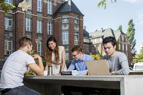 4 Studenten sitzen vor der Biomensa an einem Tisch, vor ihnen steht ein Laptop.