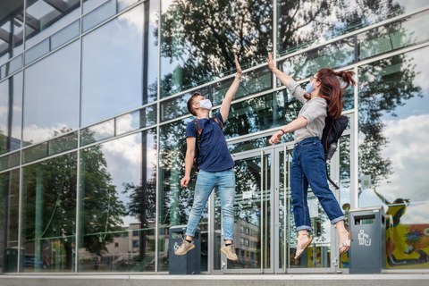 Ein Student und eine Studentin springen vor dem Hörsaalzentrum ein wenig in die Höhe.