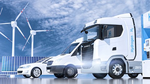 Weiße Autos vor hellblauem HImmel v.l. ein PKW, ein Kleinbus und ein LKW inmitten von Solarpaneelen, Windrädern und Elektro-Tanksäule