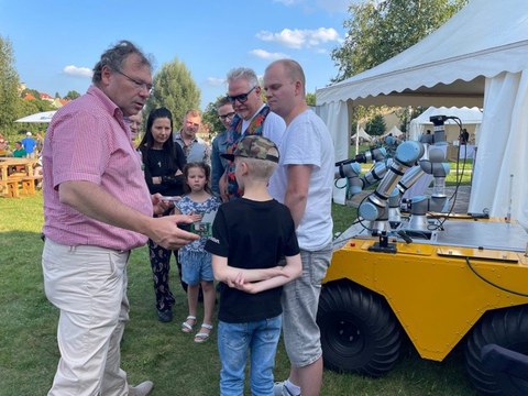 Mehrere Menschen stehen im Freien vor einem Ausstellungsstand und unterhalten sich.