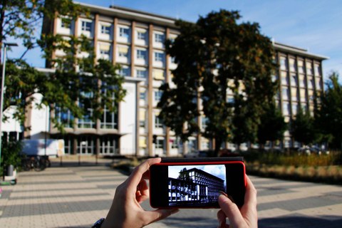 Im Hintergrund der aktuelle Andreas-Schubert-Bau. Im Vordergrund sieht man das historische Gebäude auf einem Smartphone.