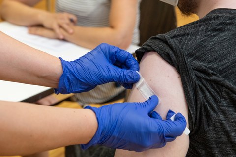 Ein Mitarbeiter bekommt nach der Impfung ein Pflaster auf den Oberarm geklebt.