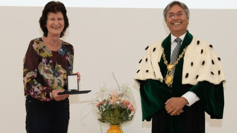 Frau Dr. Stange steht links im Bild, sie hält die Ehrenmedaille in der Hand. Der Rektor steht im Talar rechts. Beide lachen.