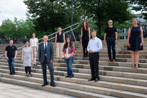 Schräger Blick auf eine Treppe im Freien, auf der Treppe stehen verteilt 10 Personen mit Blick in die Kamera.