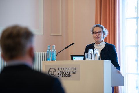 Eine Frau spricht an einem Rednerpult zu Publikum.