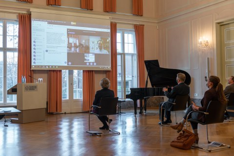 Personen verfolgen eine Präsentation auf einer Leinwand.