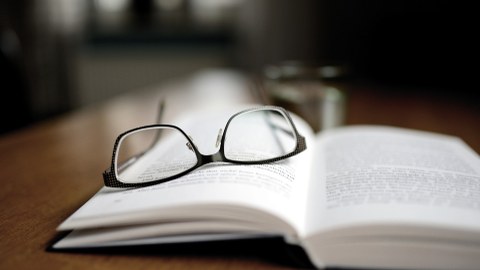 Auf einem aufgeschlagenen Buch liegt eine Brille