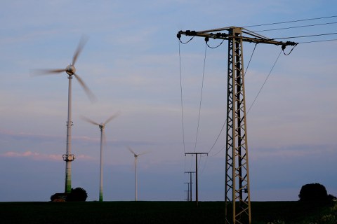 Am linken Bildrand sind Windräder zu sehen, am rechten ein Oberleitungsmast