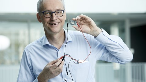 Porträtfoto von Prof. Karl Leo, er hält ein elektronisches Bauelement in der Hand.