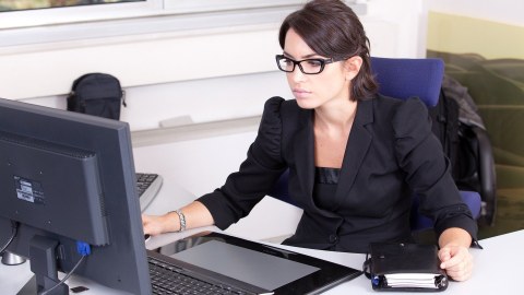 Junge, dunkelhaarige Frau mit Brille sitzt vor ihrem Computer und arbeitet