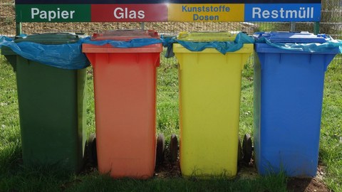 Nebeneinander stehen vier Mülltonnen aus Kunststoff, von rechts: blau, gelb, orange, dunkelgrün