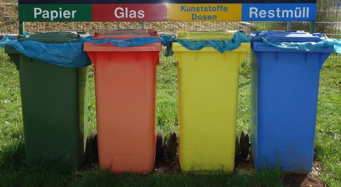 Nebeneinander stehen vier Mülltonnen aus Kunststoff, von rechts: blau, gelb, orange, dunkelgrün