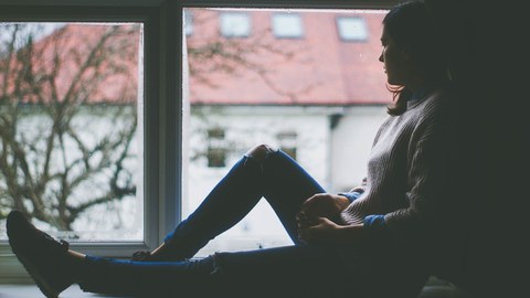 Junge Frau sitzt auf dem Fensterbrett und schaut aus dem Fenster