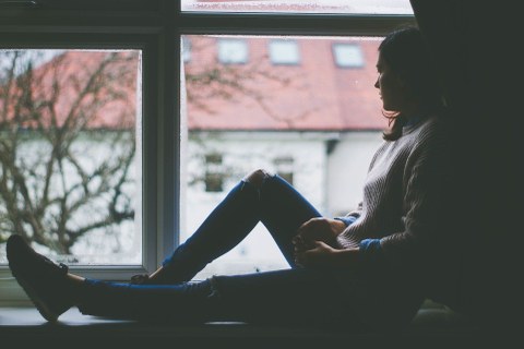 Junge Frau sitzt auf dem Fensterbrett und schaut aus dem Fenster
