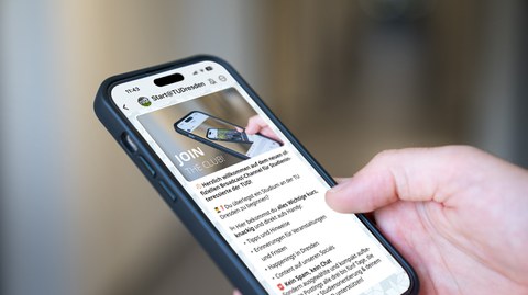 Auf dem Foto ist vor einem verschwommenem Hintergrund ein Smartphone in einer Hand zu sehen. Auf dem Smarphone sieht man den WhatsApp Broadcastchannel mit Bild und Willkommens-Text. Ins Auge fällt der Schriftszug "Join the club!"