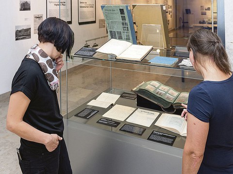 Zwei Besucherinnen betrachten eine Vitrine mit aufgeschlagenen Büchern.