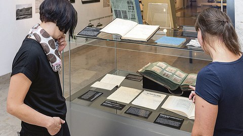 Zwei Besucherinnen betrachten eine Vitrine mit aufgeschlagenen Büchern.