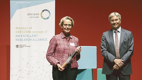 Prof. Ursula M. Staudinger hält den DRESDEN-concept-Staffelstab, den sie von ihrem Vorgänger Prof. Hans Müller-Steinhagen übergeben bekommen hat, in der Hand.